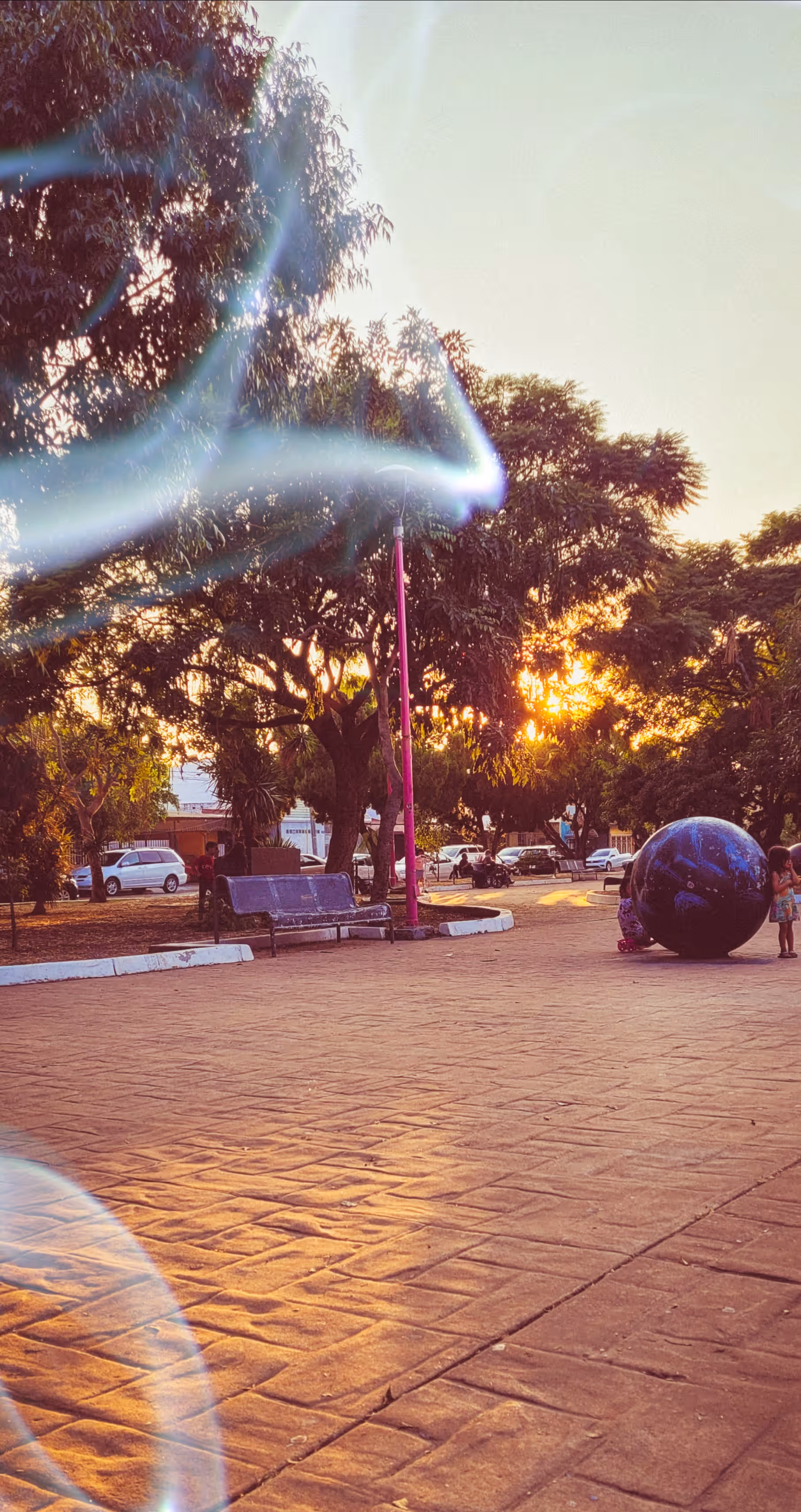Un destello atraviesa el parque y conecta por un instante el cielo, la luz urbana y una esfera terrestre.